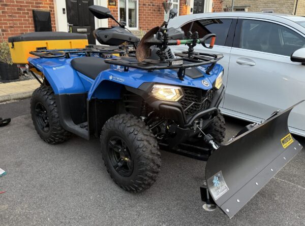 Blue Quad Bike with a Front Snowplough Parked Outside a Workshop