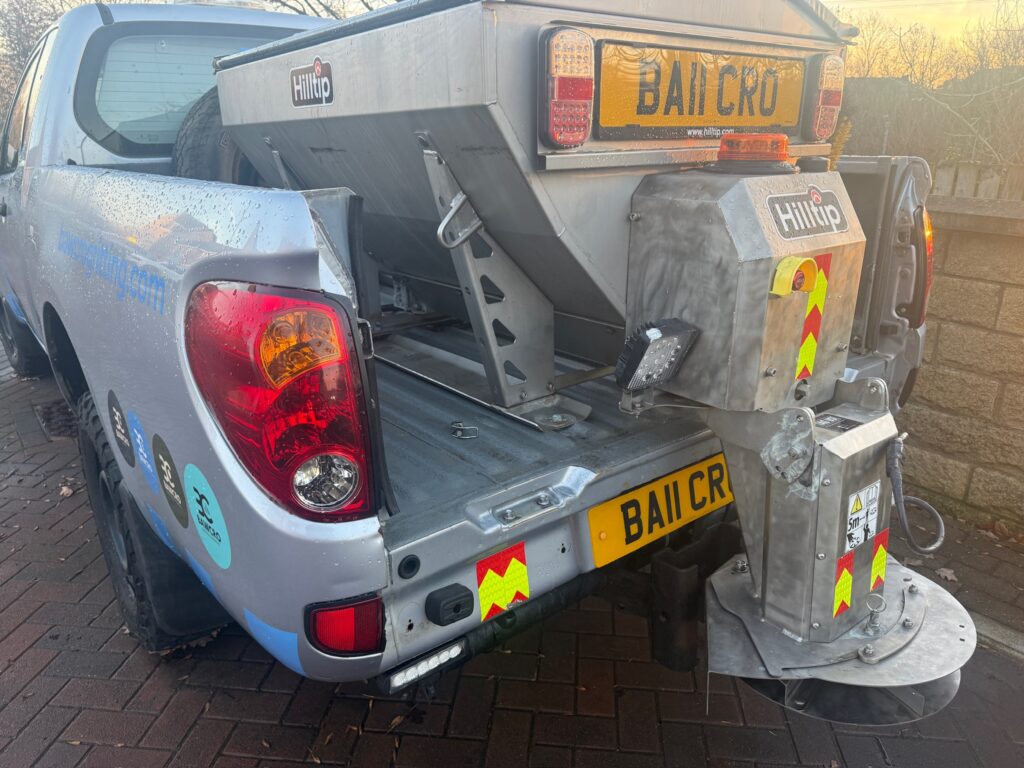 Rear of a Gray Utility Pickup with a Raised Metal Toolbox, Yellow Bailcro License Plate, Reflective Chevrons, and a Hydraulic Lift Apparatus