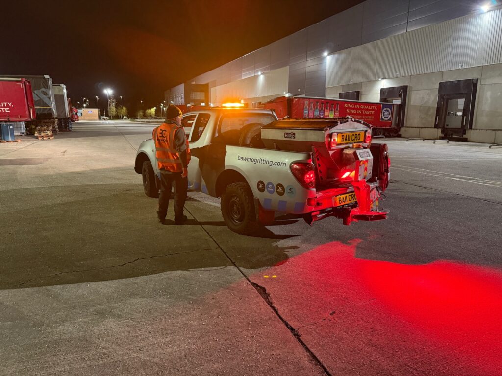 Nighttime Loading Yard with a Worker in a High-visibility Vest Standing Beside a Pickup Truck with a Flashing Orange Beacon Outside a Large Warehouse.