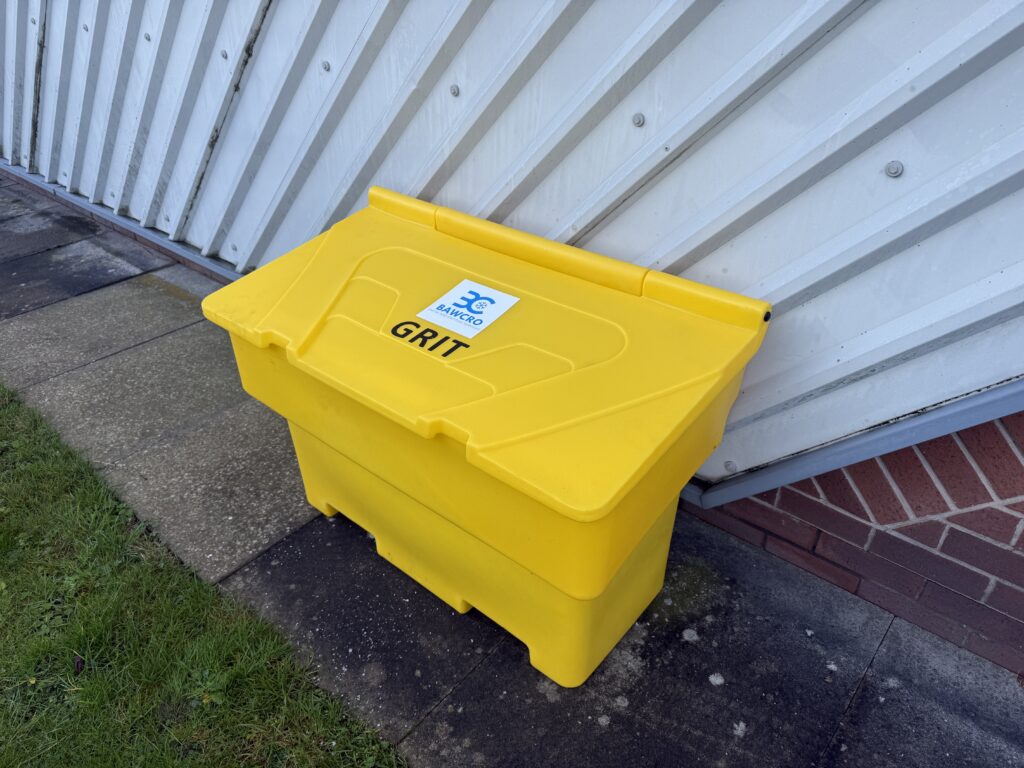Yellow Bawcro Grit Bin with Its Lid Closed Beside a Corrugated Wall